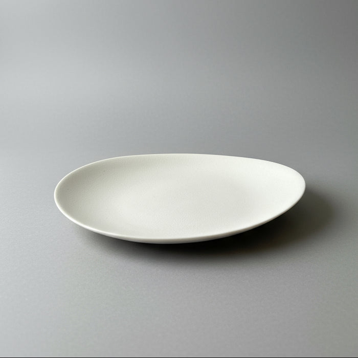 A white oval-shaped porcelain tea plate displayed on a wooden surface.