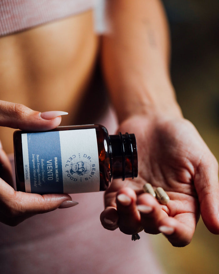 Woman holding a dark glass Dr. Sebi herbal supplement bottle in natural sunlight.