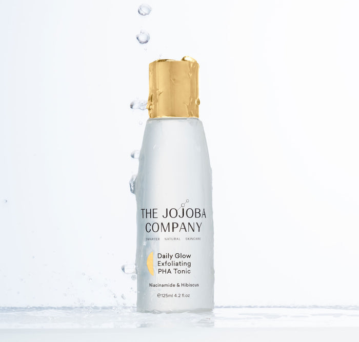 A skincare product by The Jojoba Company with water droplets splashing around it.