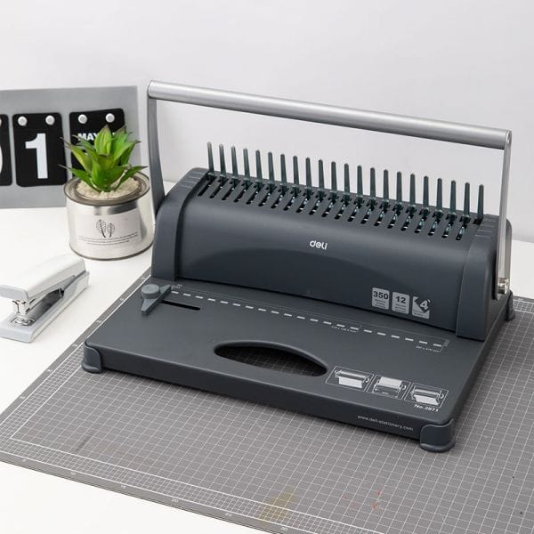 Gray office binding machine on a desk with a plant and calendar in the background
