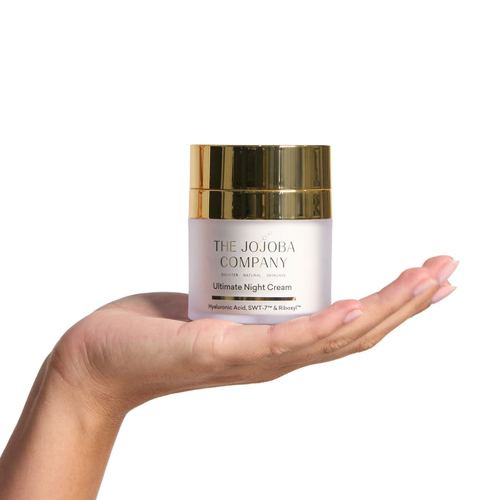 Hand holding a jar of 'The Jojoba Company' Ultimate Night Cream on a white background