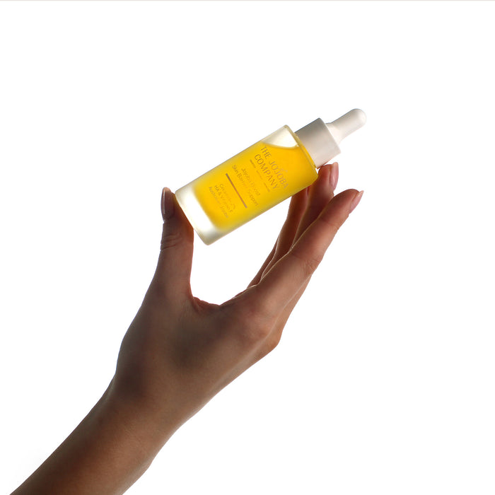 Hand holding a bottle of yellow liquid The Jojoba Company Jojoba Boost Boost Skin Barrier Support Serum on a white background
