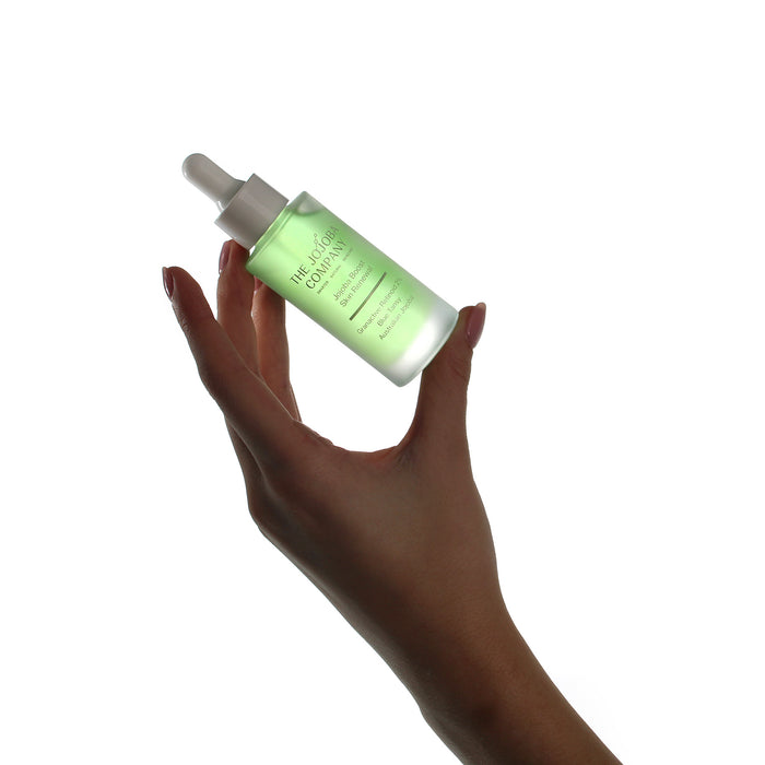 Hand holding a green skincare serum bottle with dropper on a white Jojoba Boost Skin Renewal background