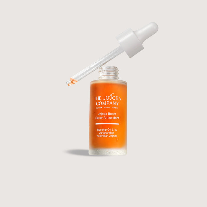 Skincare dropper bottle with orange liquid and white cap on a light gray  background from The JOjoba COmpany and the Jojoba Boost Super Antioxidant Serum