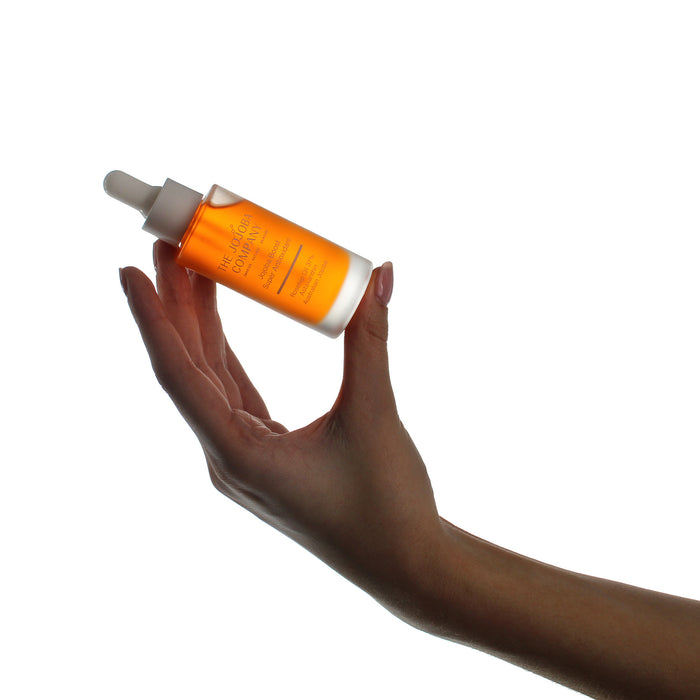 Hand holding a bottle of The Jojoba Company Jojoba Boost Super Antioxidant orange bottle with a dropper on a white background