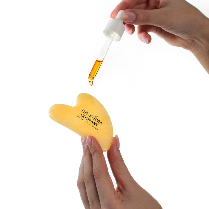 Heart-shaped yellow bottle with dropper held by a hand on a white background