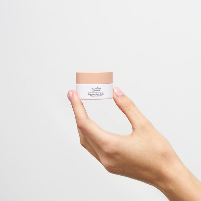 Hand holding The Jojoba Company Overnight Multi-biotic Moisture Cream packaging on a white background