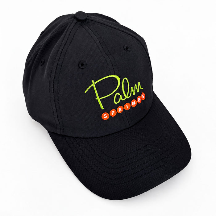 A black baseball cap featuring a curved brim and embroidered 'Palm Springs' text on the front, with 'Palm' in neon yellow-green script and 'SPRINGS' in orange-red oval letters, shown on a clean white background.