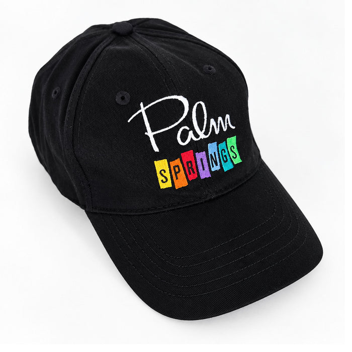 A black baseball cap featuring embroidered text that reads 'Palm Springs' in white script and colorful block letters, shown on a plain white background.