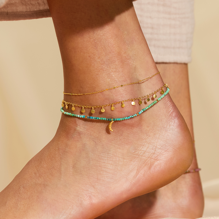 Stylishly layered anklets featuring the Walk with Joy Coin Chain Anklet, showcasing a fusion of colors and textures. This spiritual jewelry piece resonates with the energies of the sun and moon, ideal for yoga enthusiasts and those seeking meaningful adornments for their spiritual journey.